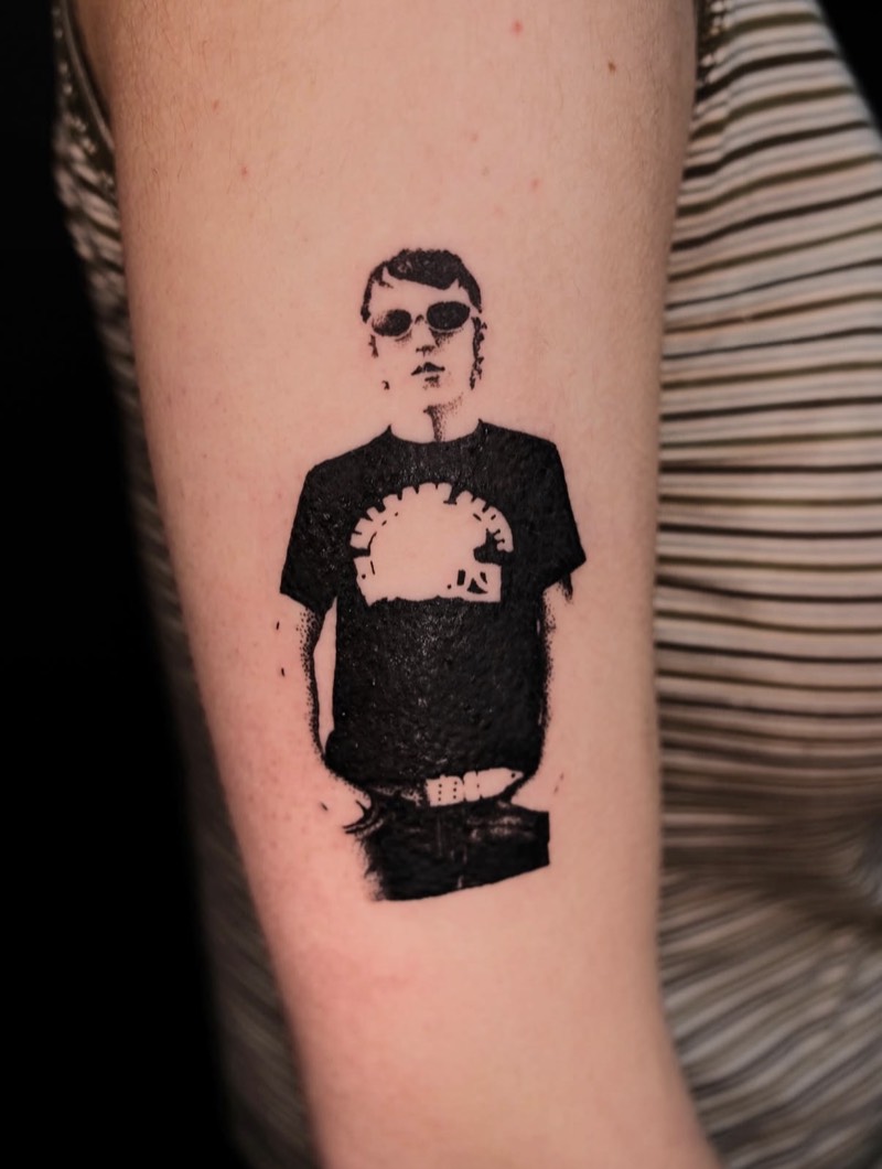 Completed tattoo on the upper arm: a figure in sunglasses and a black T-shirt, in solid black and stippled shading
