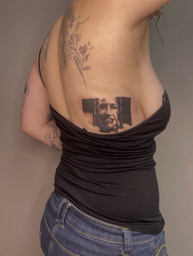 Completed tattoo on the lower back: a grinning face behind bars, in black and grey stippling