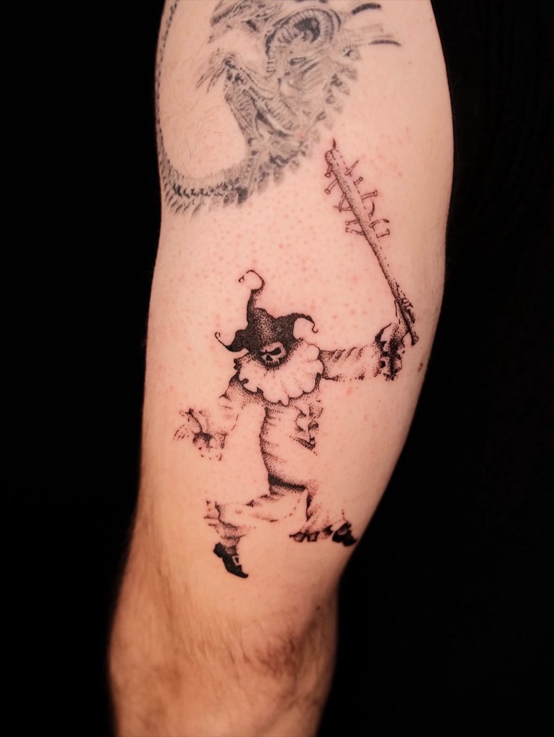 Completed tattoo on the arm: a jester with a skull face swinging a nail-studded bat, in dotwork