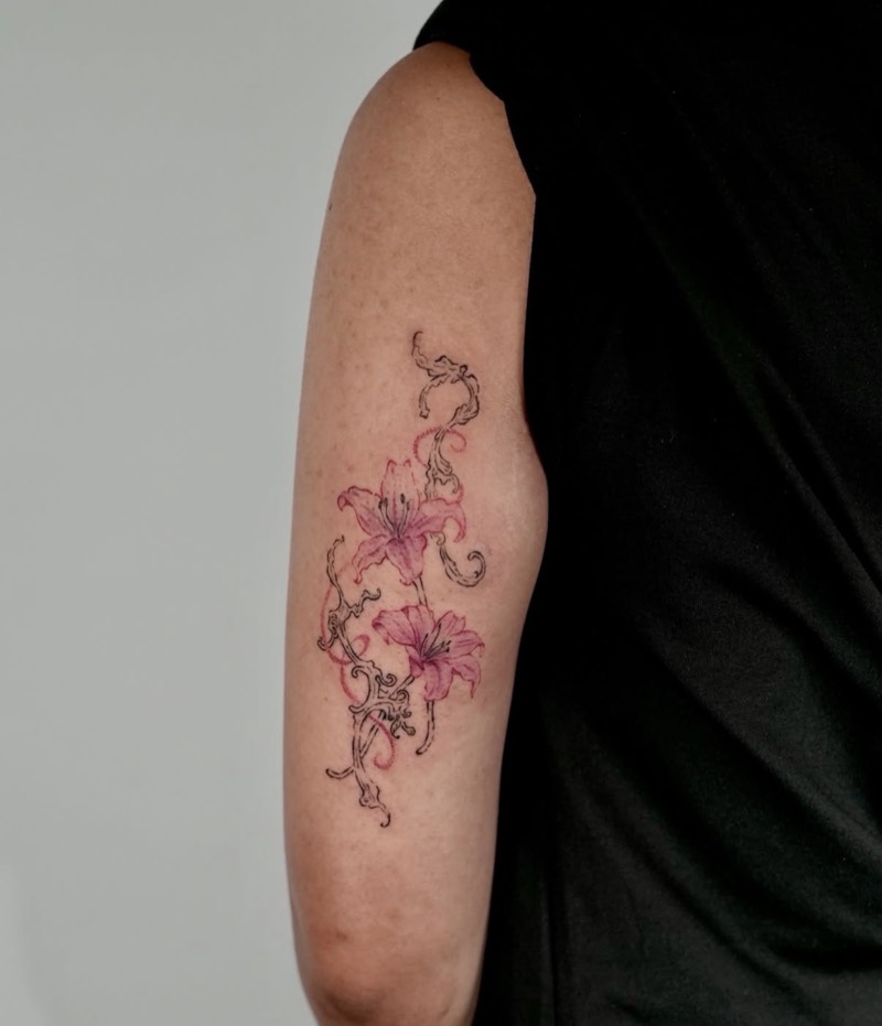 Completed tattoo on the upper arm: two pink lilies on fine black ornamental vines with red dotted swirls