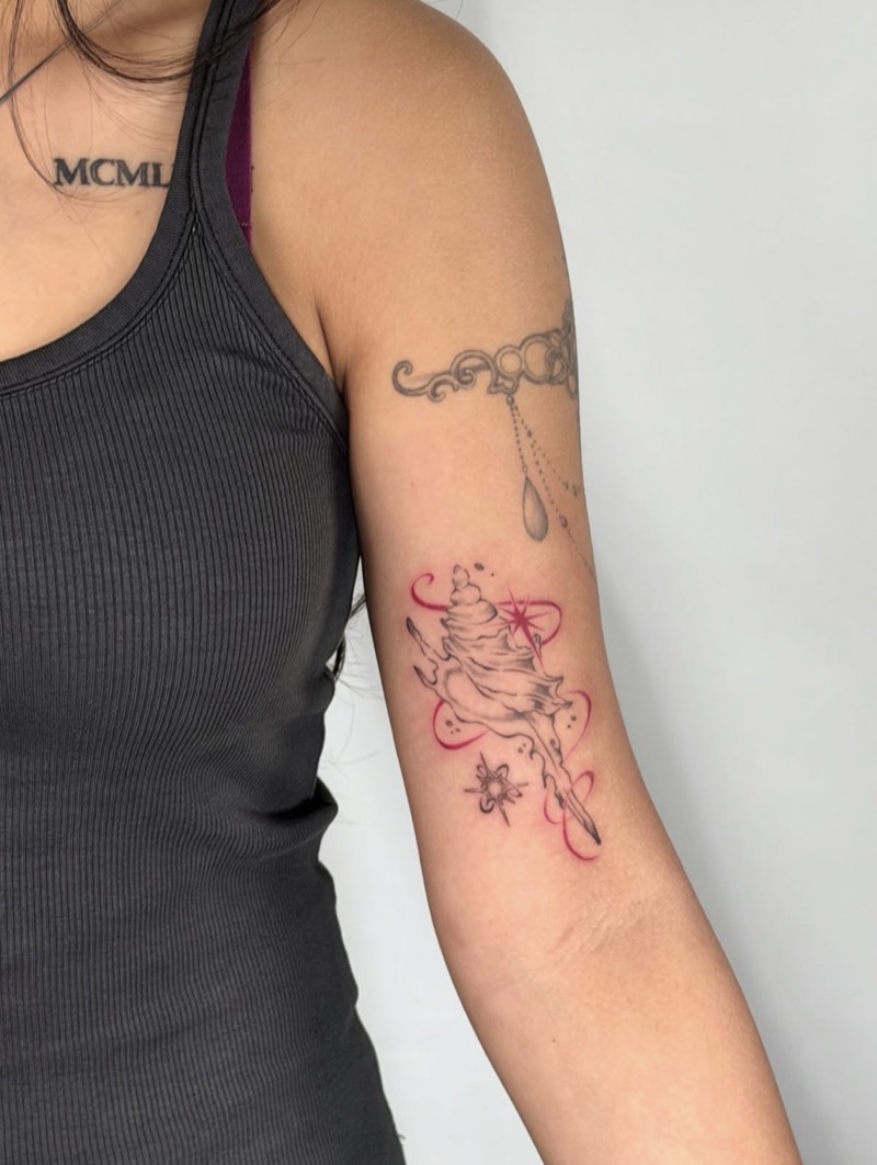 Completed tattoo on the upper arm: a spiral seashell in black and grey with red ribbon swirls and sparkles