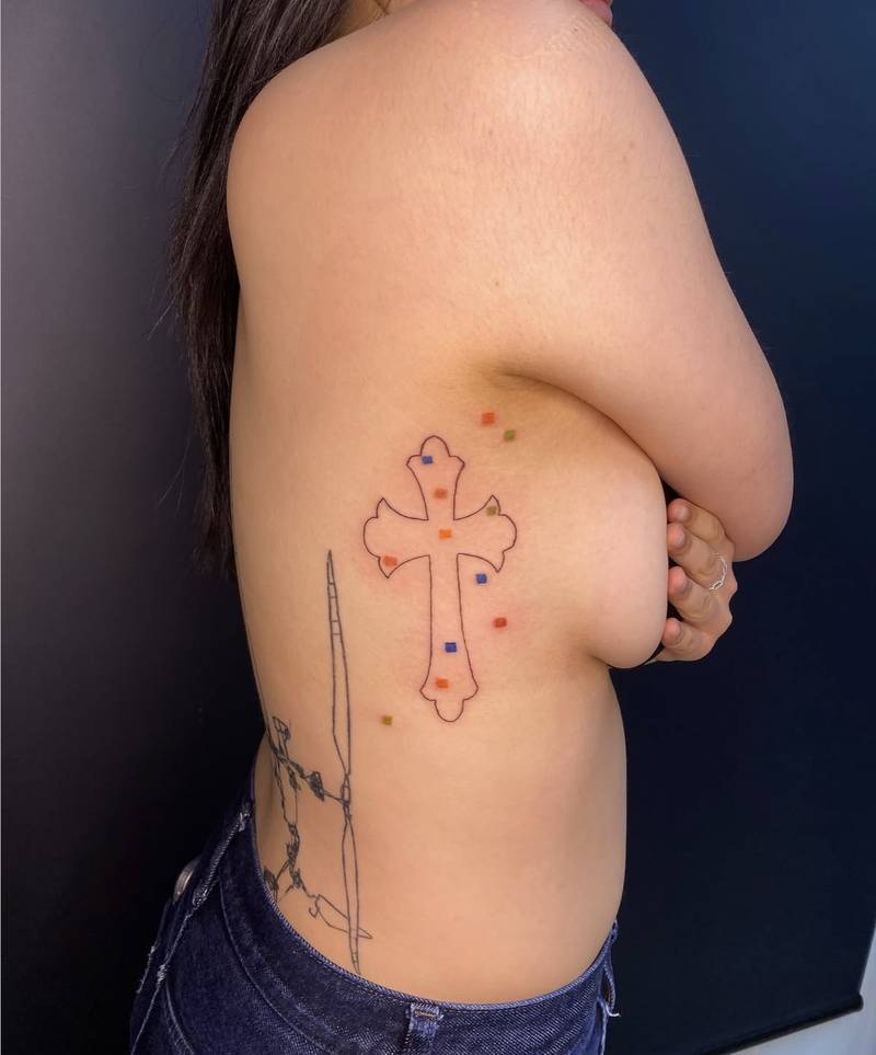 Completed tattoo on the ribs: an outlined ornamental cross surrounded by small red, orange, green and blue squares
