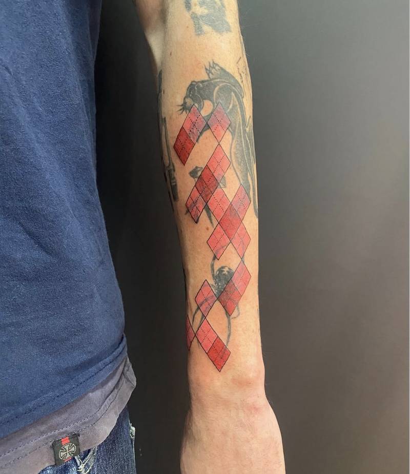 Completed tattoo on the forearm: a trailing pattern of red and pink diamonds with fine black outlines and dotted details