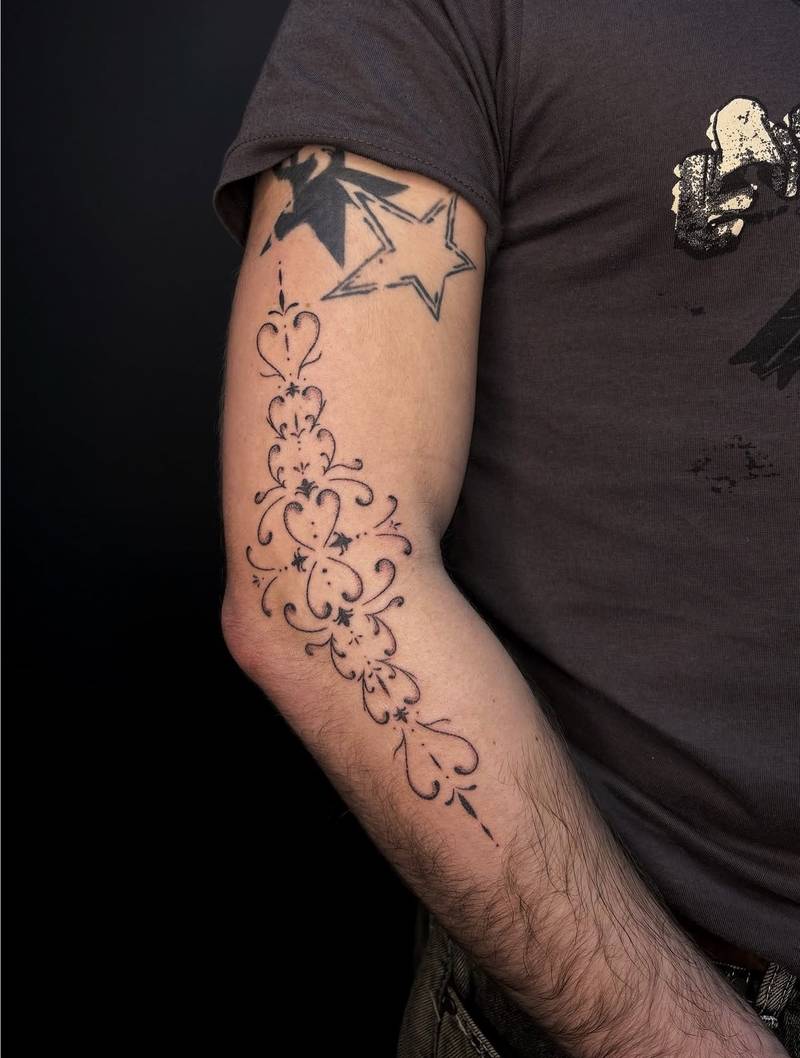 Completed tattoo along the arm and elbow: a flowing ornamental pattern of hearts, curling lines and small dark accents