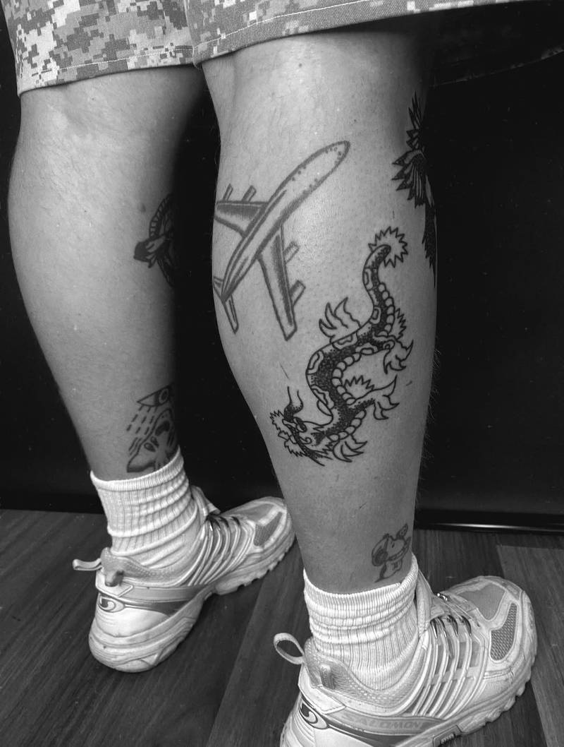 Completed tattoo on the calf: a curling dragon with clawed feet and a spiked tail, in black linework and stippled shading
