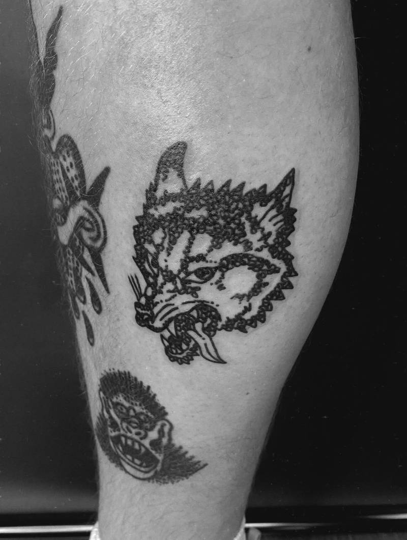 Completed tattoo on the leg: a snarling wolf head with pointed ears, bared teeth and a curling tongue, in textured black linework
