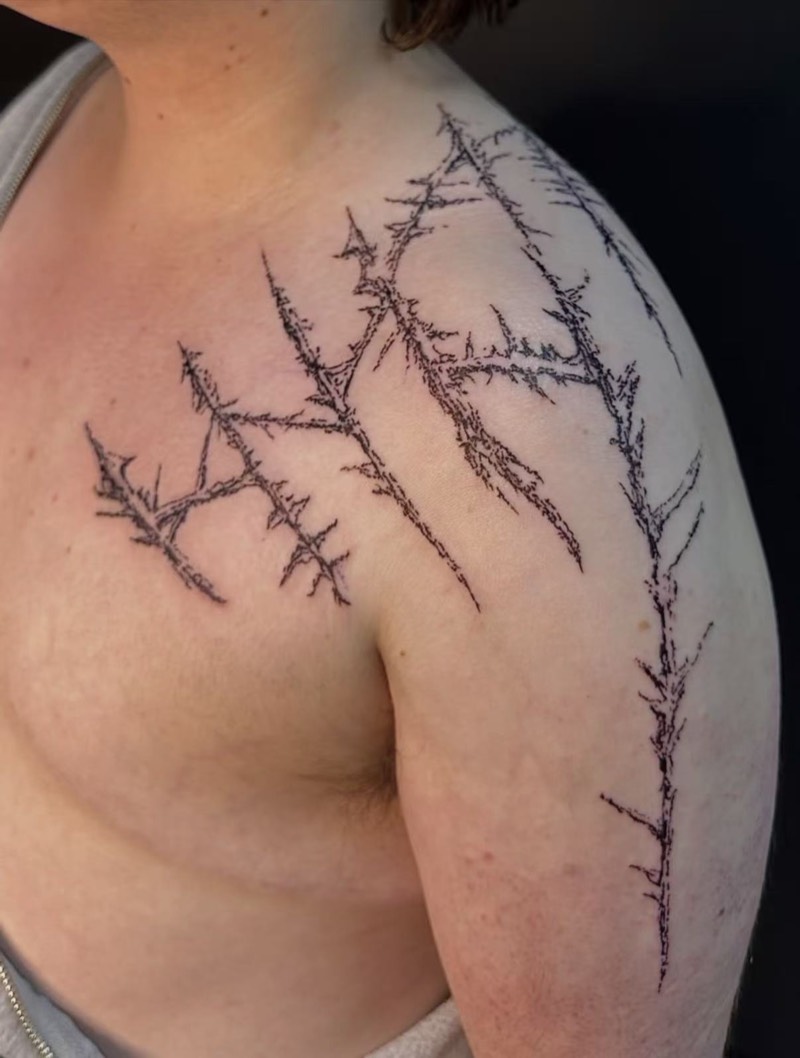 Completed tattoo on the chest and shoulder: thorned branches in scratchy fine black line running over the shoulder and down the arm