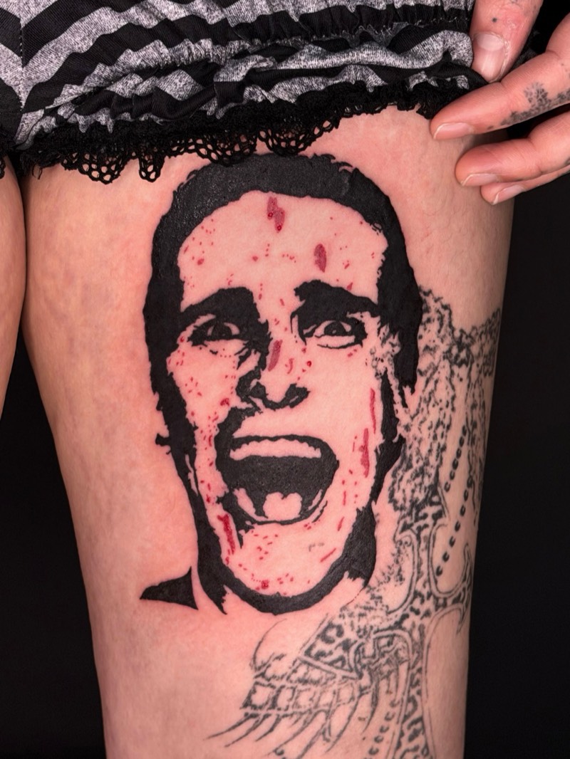 Completed tattoo on the thigh: a screaming face in bold black with red spatter
