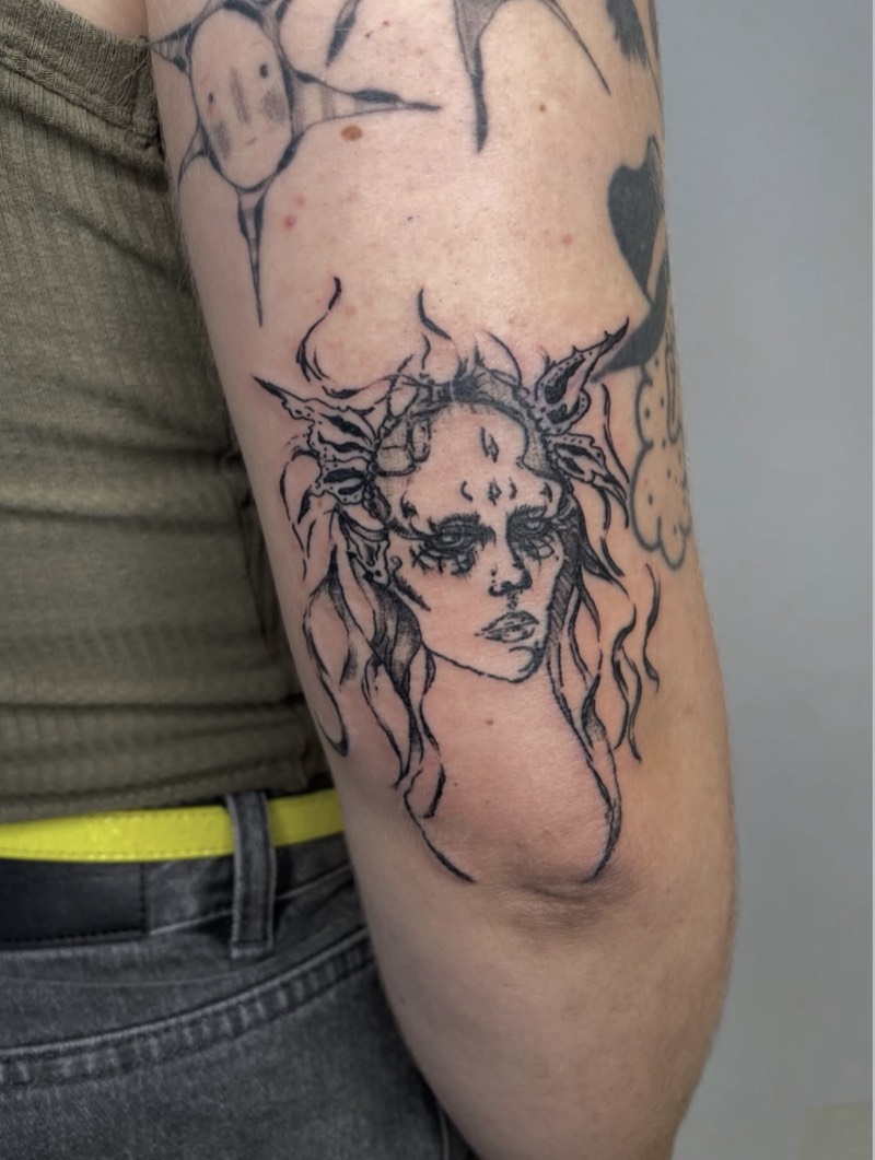 Completed tattoo on the elbow: a woman's face with flowing hair and a spiky crown, in sketchy black line