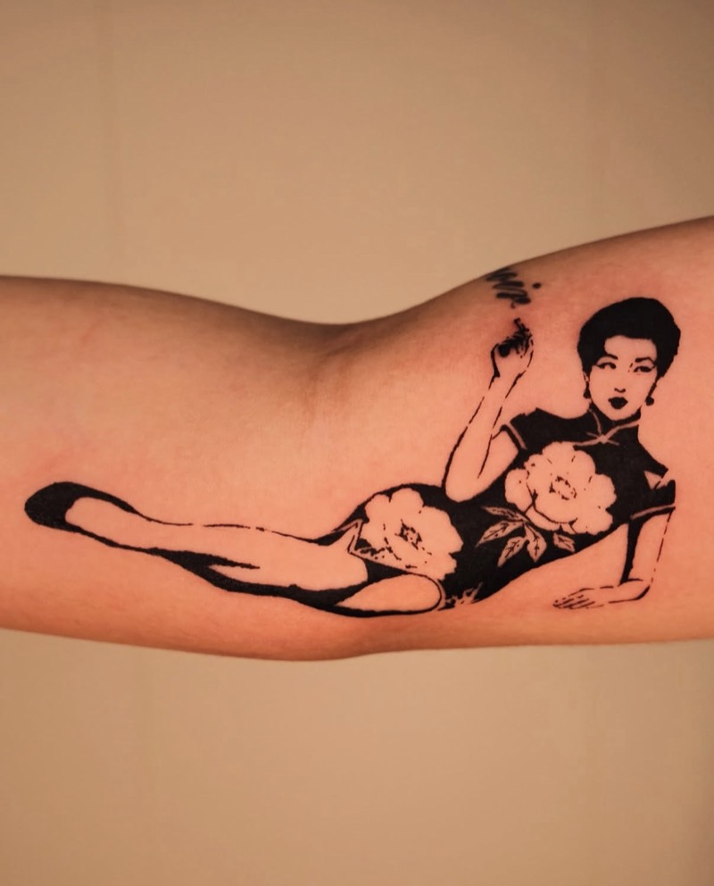 Completed tattoo on the upper arm: a reclining woman in a black high-collared dress with white peonies, holding a cigarette, in solid black