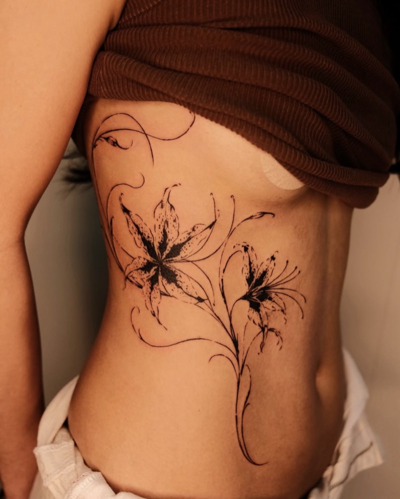 Completed tattoo on the ribs: two spotted lilies on long curling stems, in fine black line